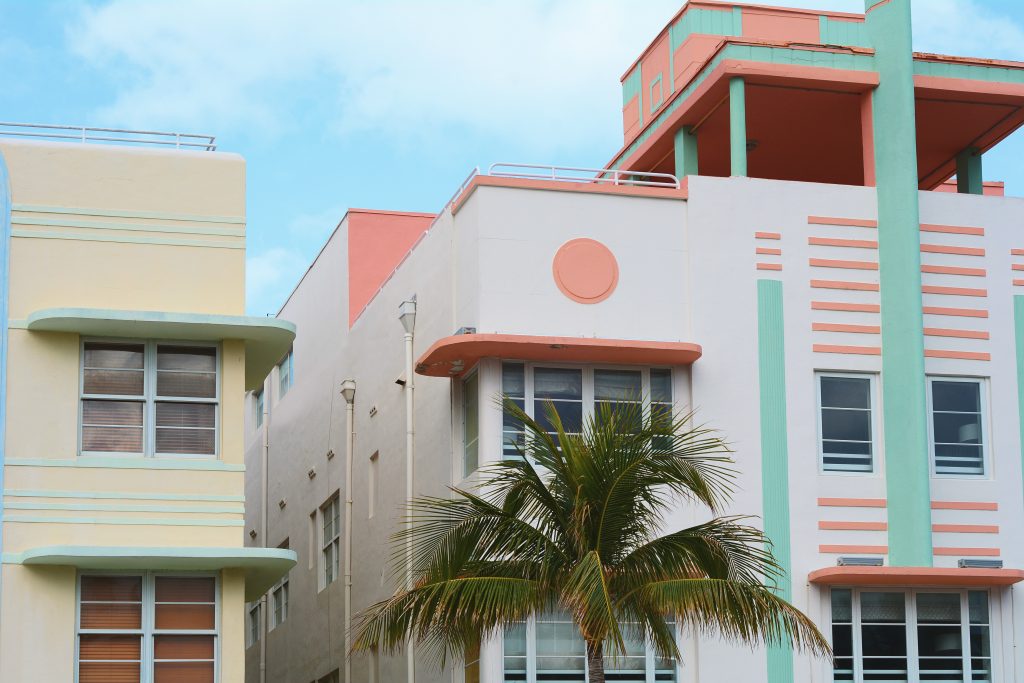 An image of a building showcasing the art deco style. It is a fun, pink, ornamented building with a palm tree in front.