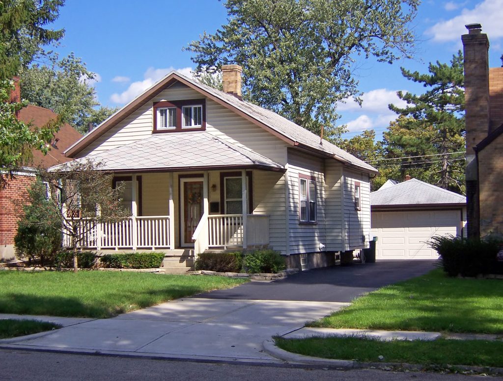 An image of a standard bungalow home. It is a one and a half story home with white siding, a porch, and a garage in the back.