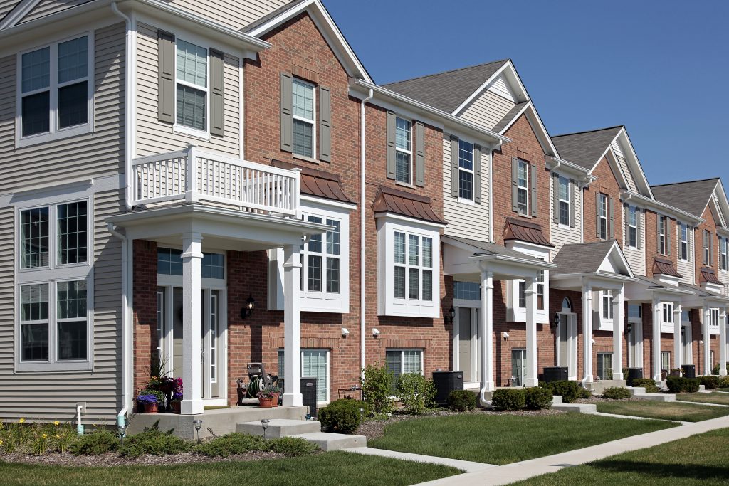 A row of two or three story townhomes. The townhomes are each half brick and half siding, with covered entryways. 